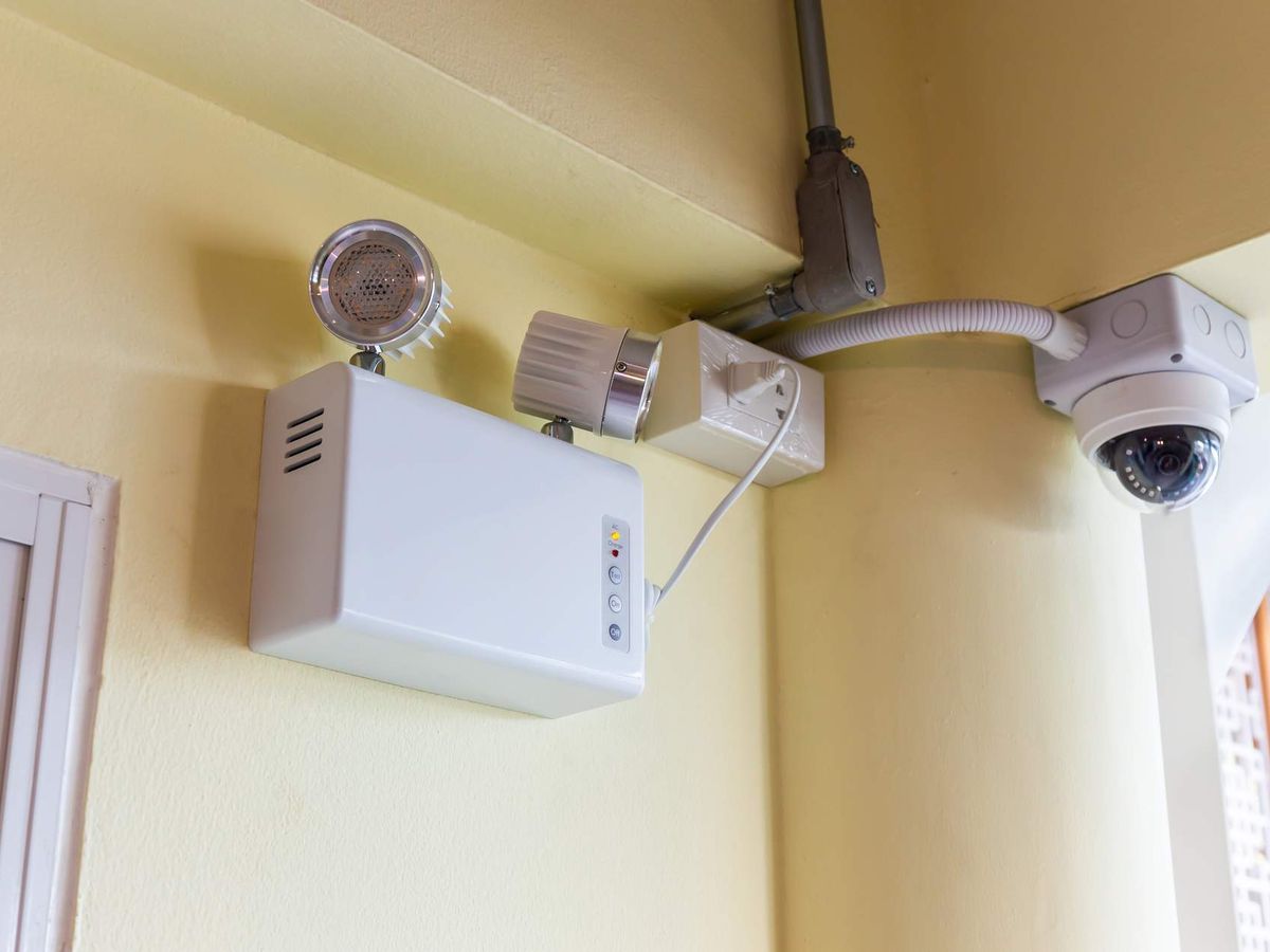 A wall-mounted twin-lamp emergency light and a dome security camera in the corner of a room
