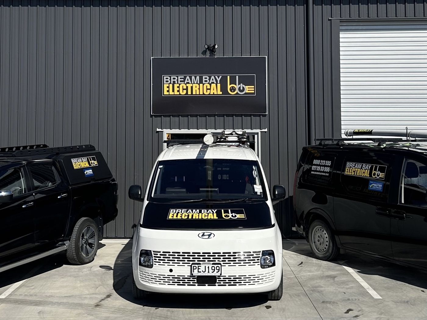 The Bream Bay Electrical ute and two vans lined up in front of the workshop