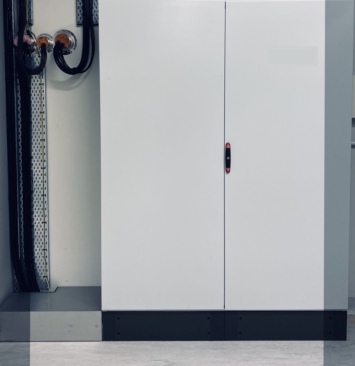 A closed floor-standing grey electrical enclosure with cable tray running up the wall beside it