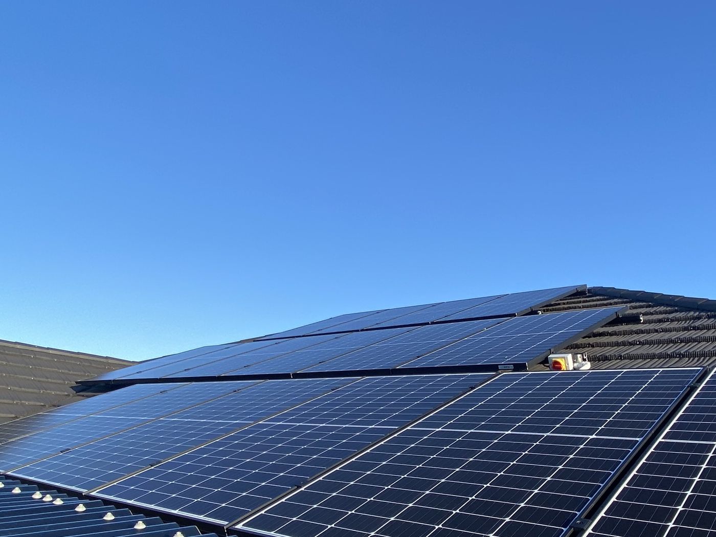 Rows of solar panels on a corrugated iron roof under a clear blue sky