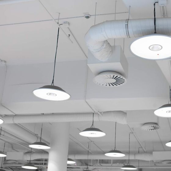 White pendant lights, a round air diffuser and exposed ducting on a commercial ceiling